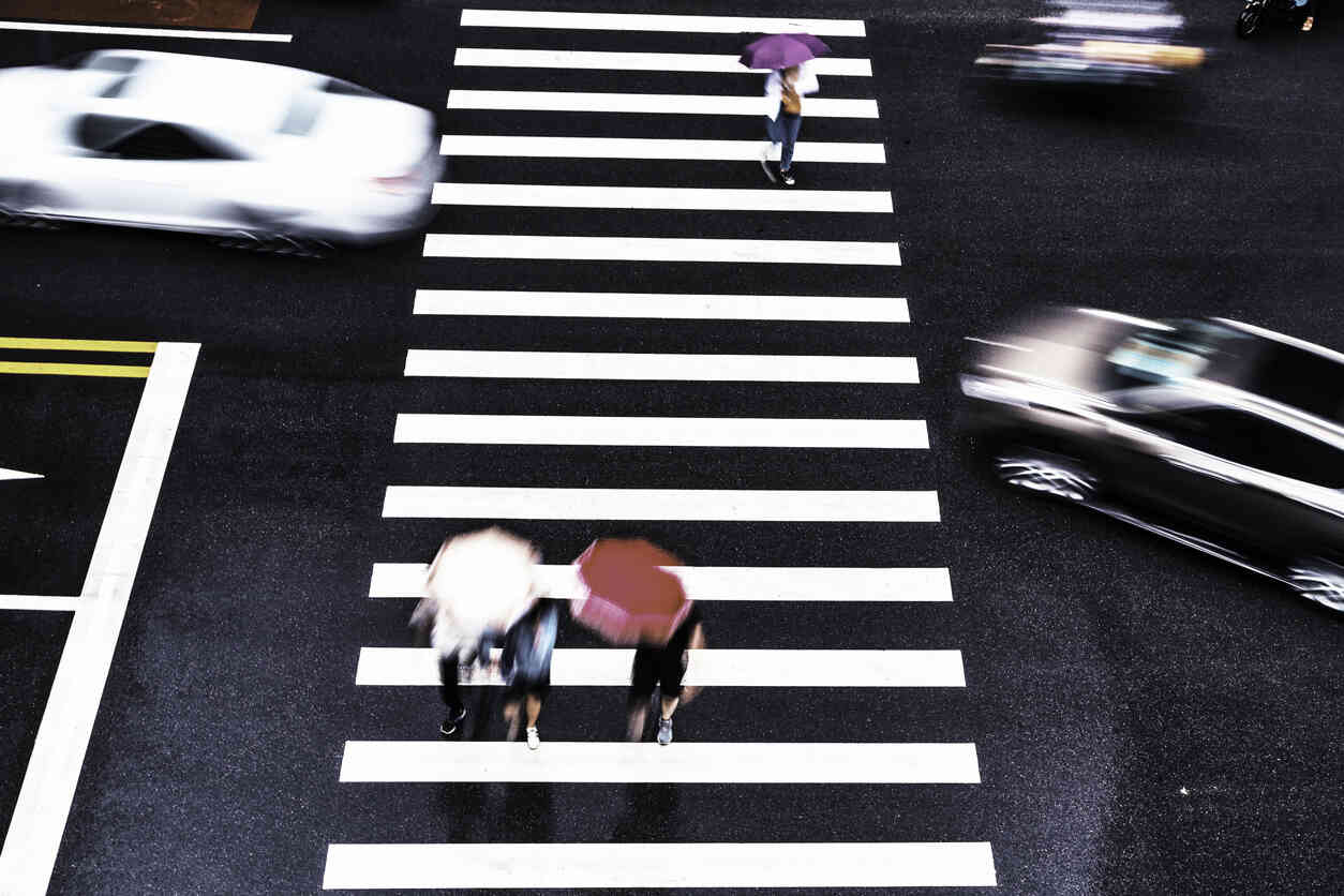 Three individuals walking on a crosswalk while vehicles pass quickly, depicting a common urban pedestrian environment in Albuquerque.