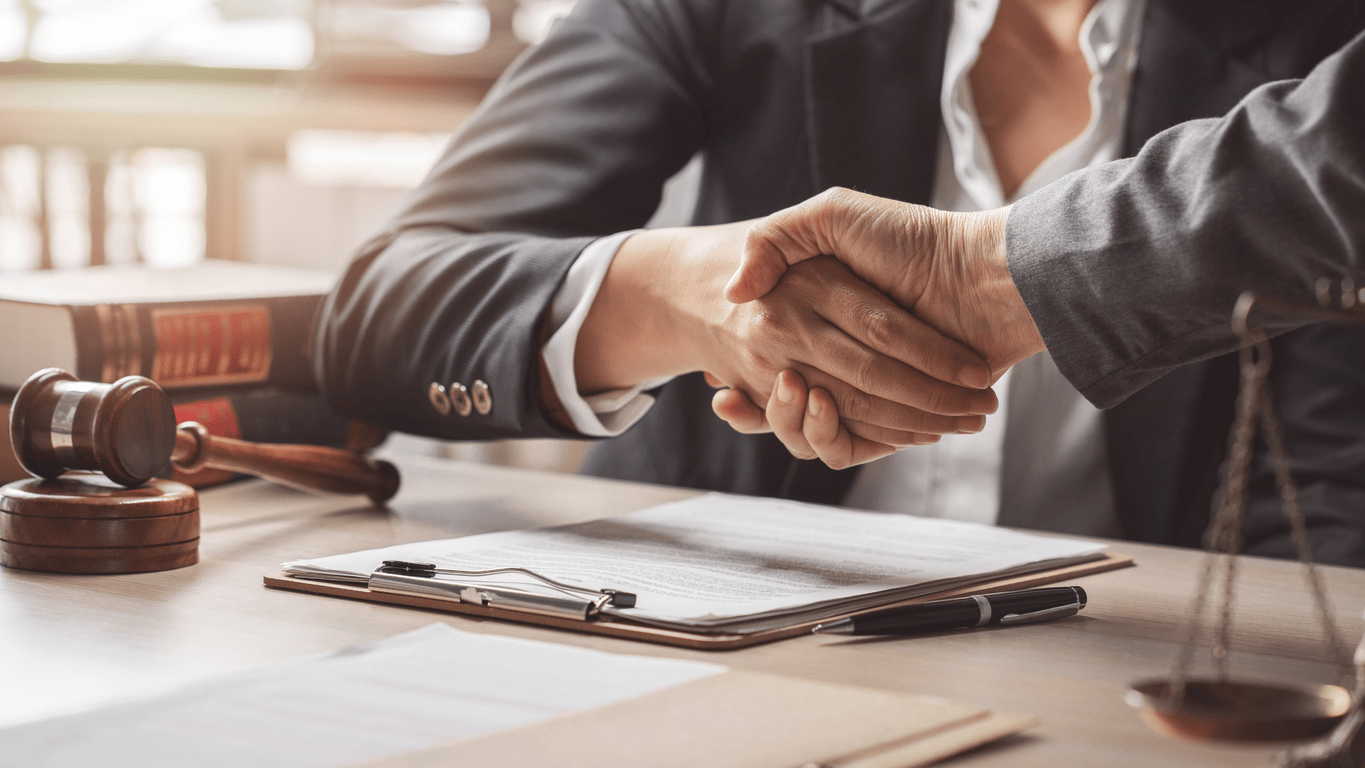 Lawyer is shaking hands over legal documents and a gavel, indicating a legal agreement