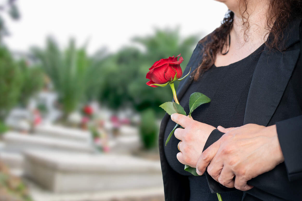 A person holding a red rose stands solemnly at a cemetery, symbolizing grief and loss, reflecting on wrongful death.